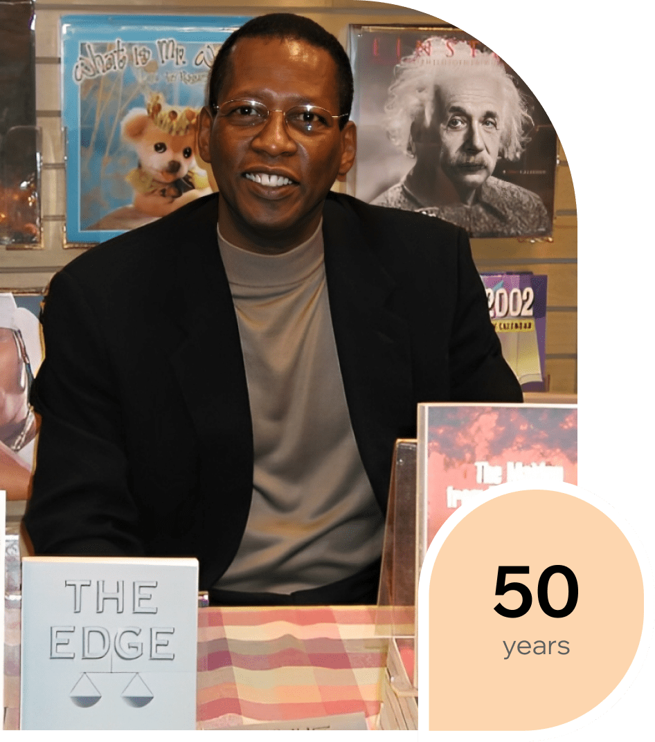 Man sitting at a table with books and posters behind him.